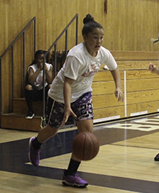 A woman dribbles the basketball on a court.