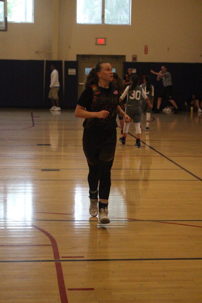 A girl is walking on the court with her basketball.