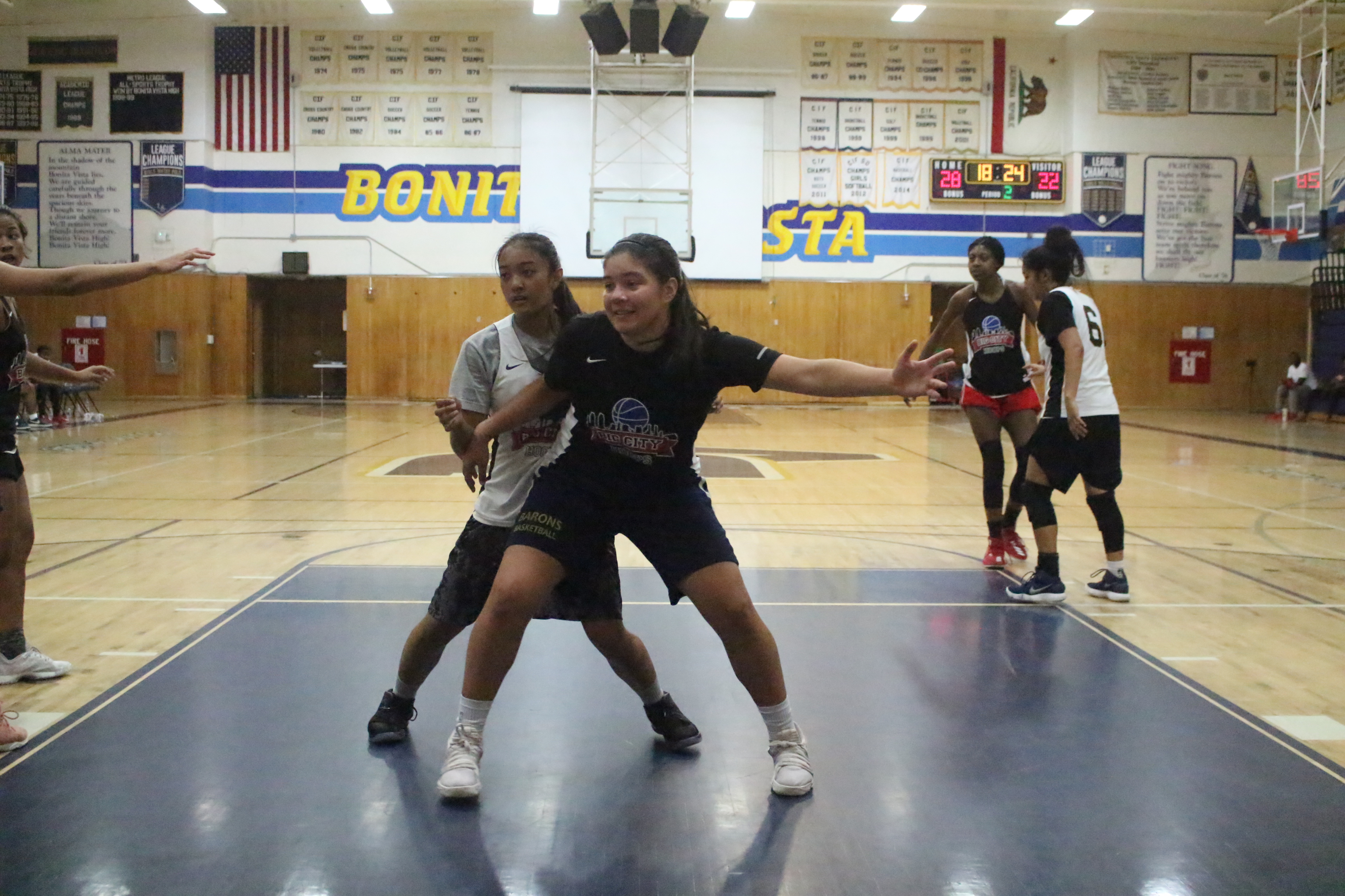Two girls are playing basketball in a gym.