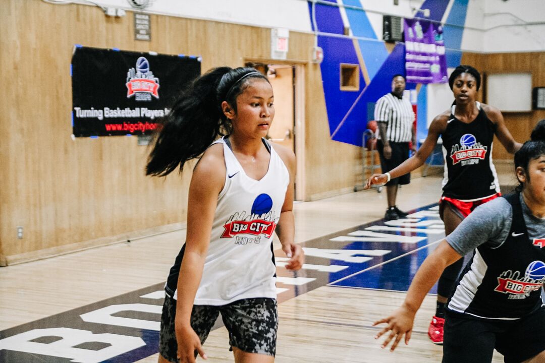 A girl in white shirt playing basketball on court.