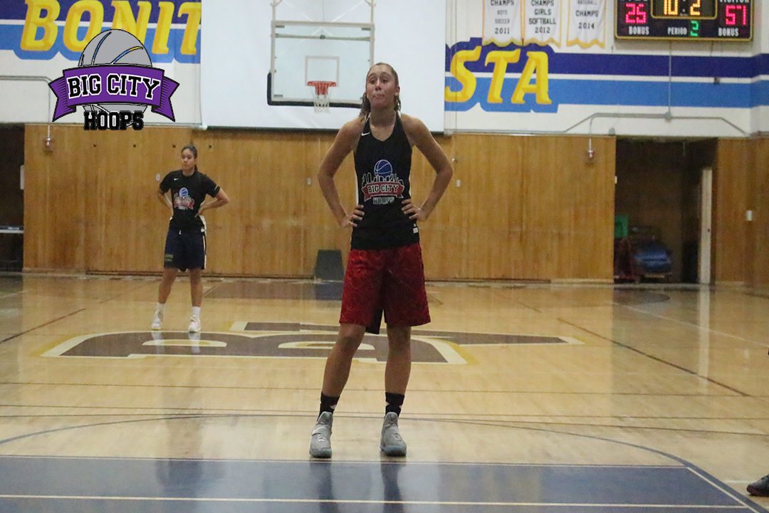 A girl standing on the court with her hands behind her back.